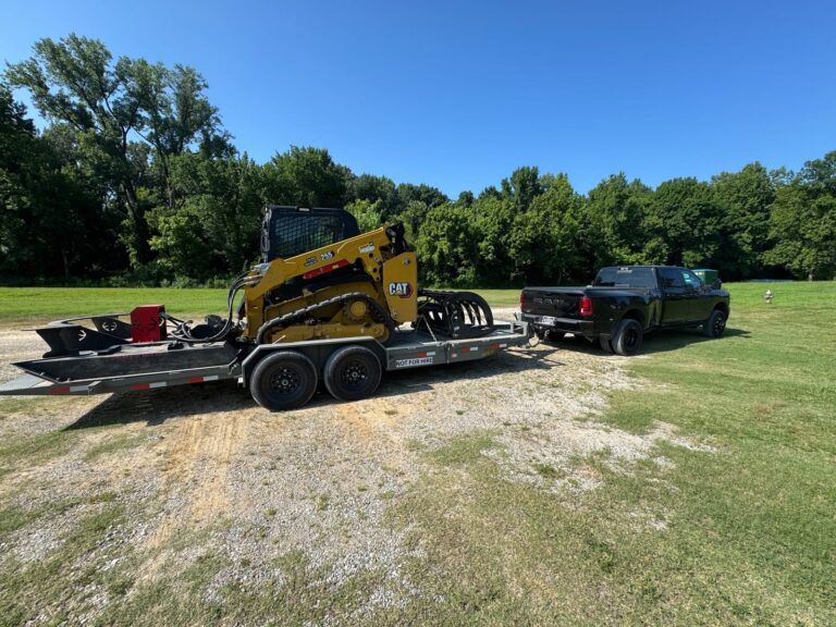CAT 255 compact track loader with 82-inch brush cutter on a trailer, arriving at a pond levee clearing job in Millington, Tennessee